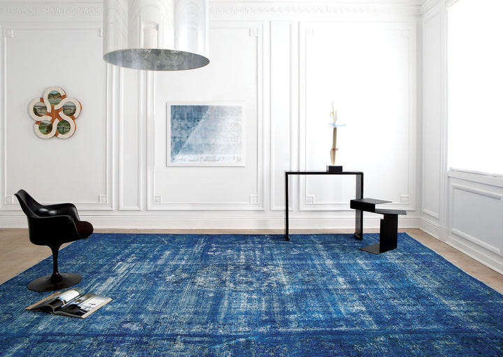 In front of a white wall, a large blue handwoven rug sets the scene for a modern yet elegant space. 