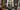 The picture depicts a large living room in modern style with an elegant layout. The room has high ceilings and one large modern metal lighting. The walls are pa