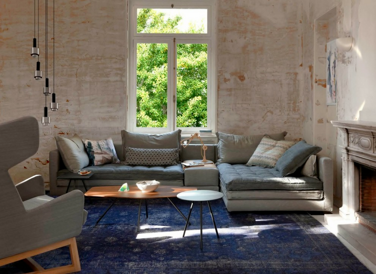 a modern, minimalist living room with a rustic touch. The layout features a large, L-shaped sectional sofa adorned with various patterned cushions, positioned a