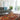 Showcasing a modern living room with a minimalist style. It features a grey mid-century modern sofa with tufted cushions. The sofa is placed on a vibrant, intricately patterned Turkish rug dominated by shades of red, blue and beige. 